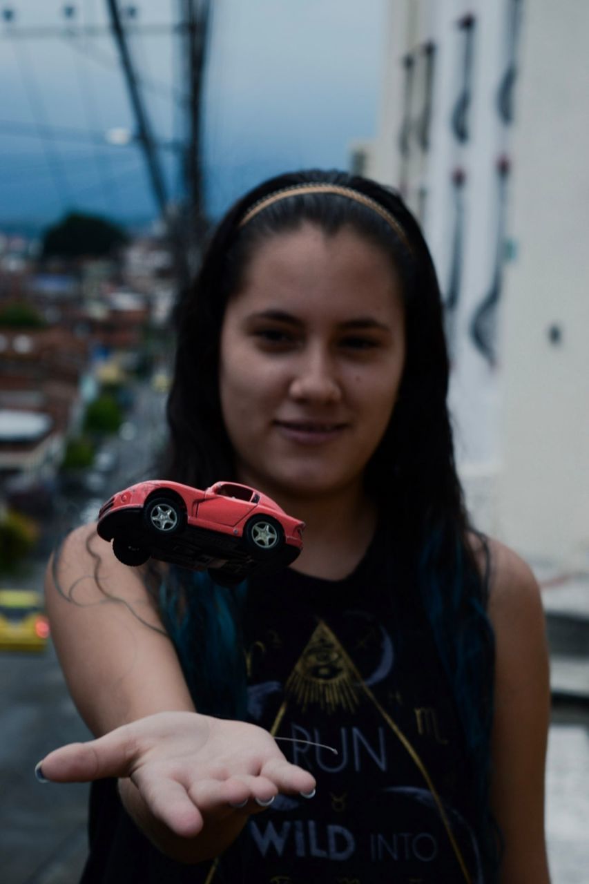 Young woman playing with toy car on roadside in city