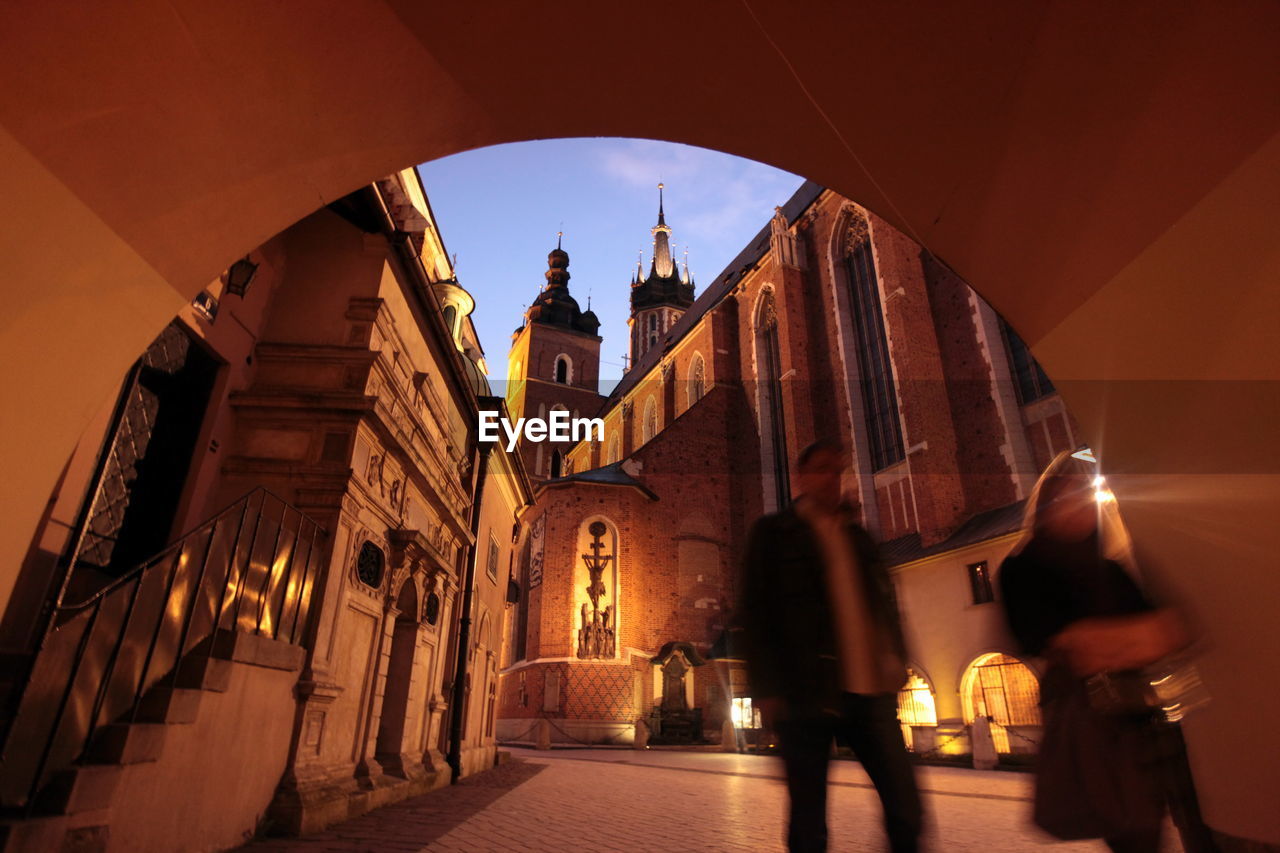 People walking on street by tunnel against wawel cathedral at dusk