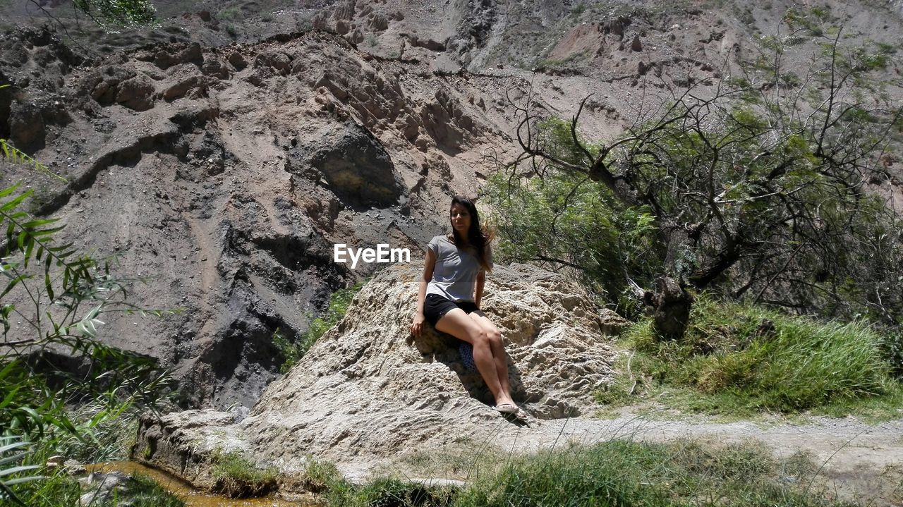 Woman looking away while sitting against rock formation