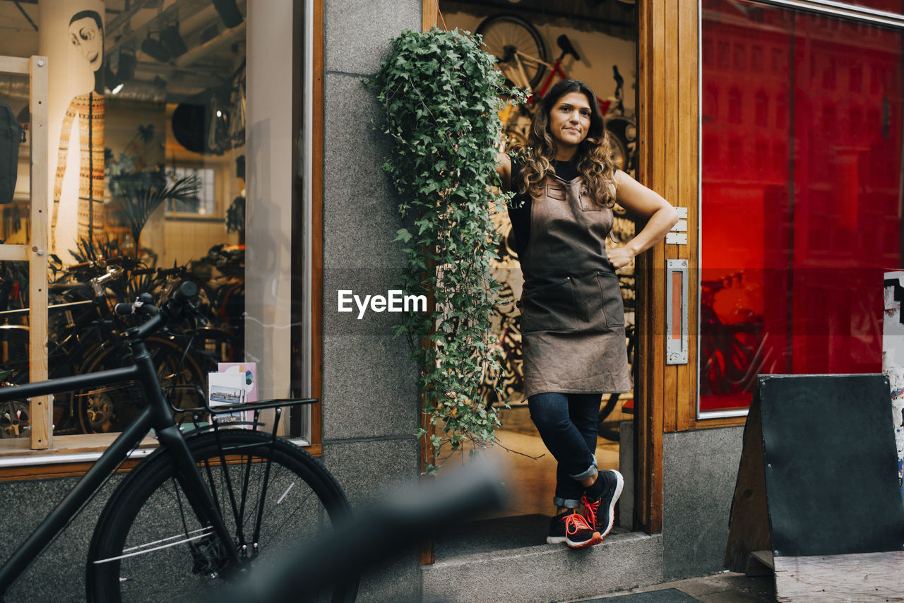 Businesswoman with hand on hip standing on doorway of bicycle shop