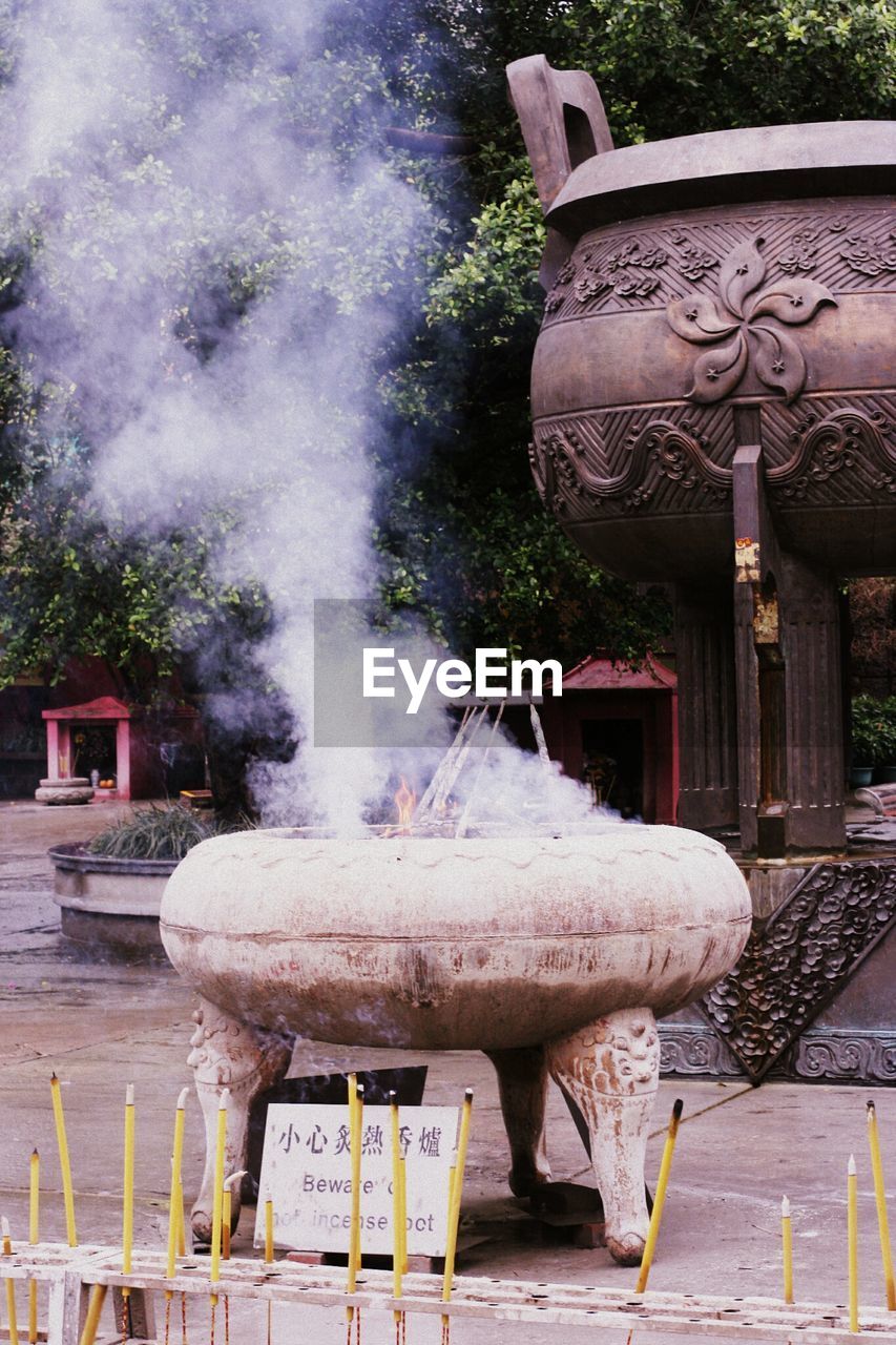 Smoke swirling out of joss sticks in an incense pot outdoors