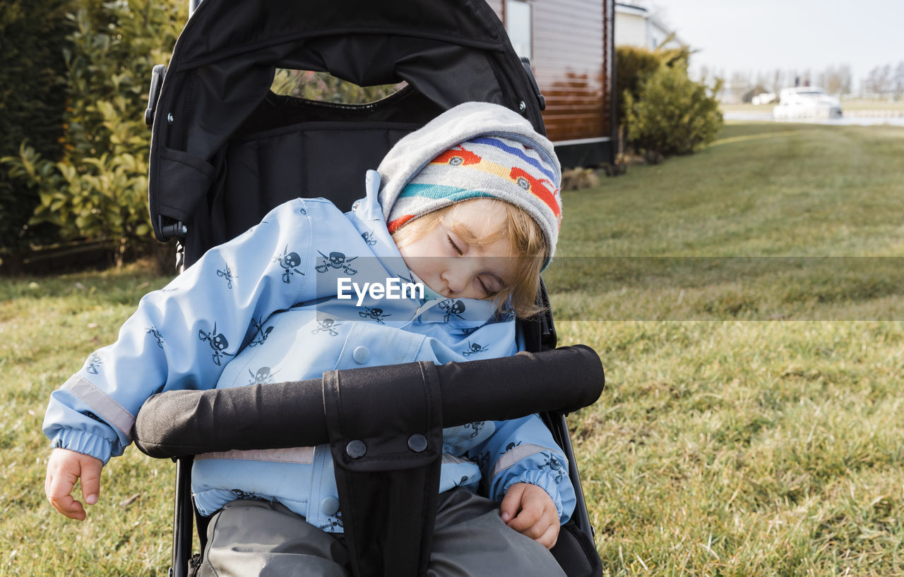 Cute boy sleeping on baby stroller at lawn