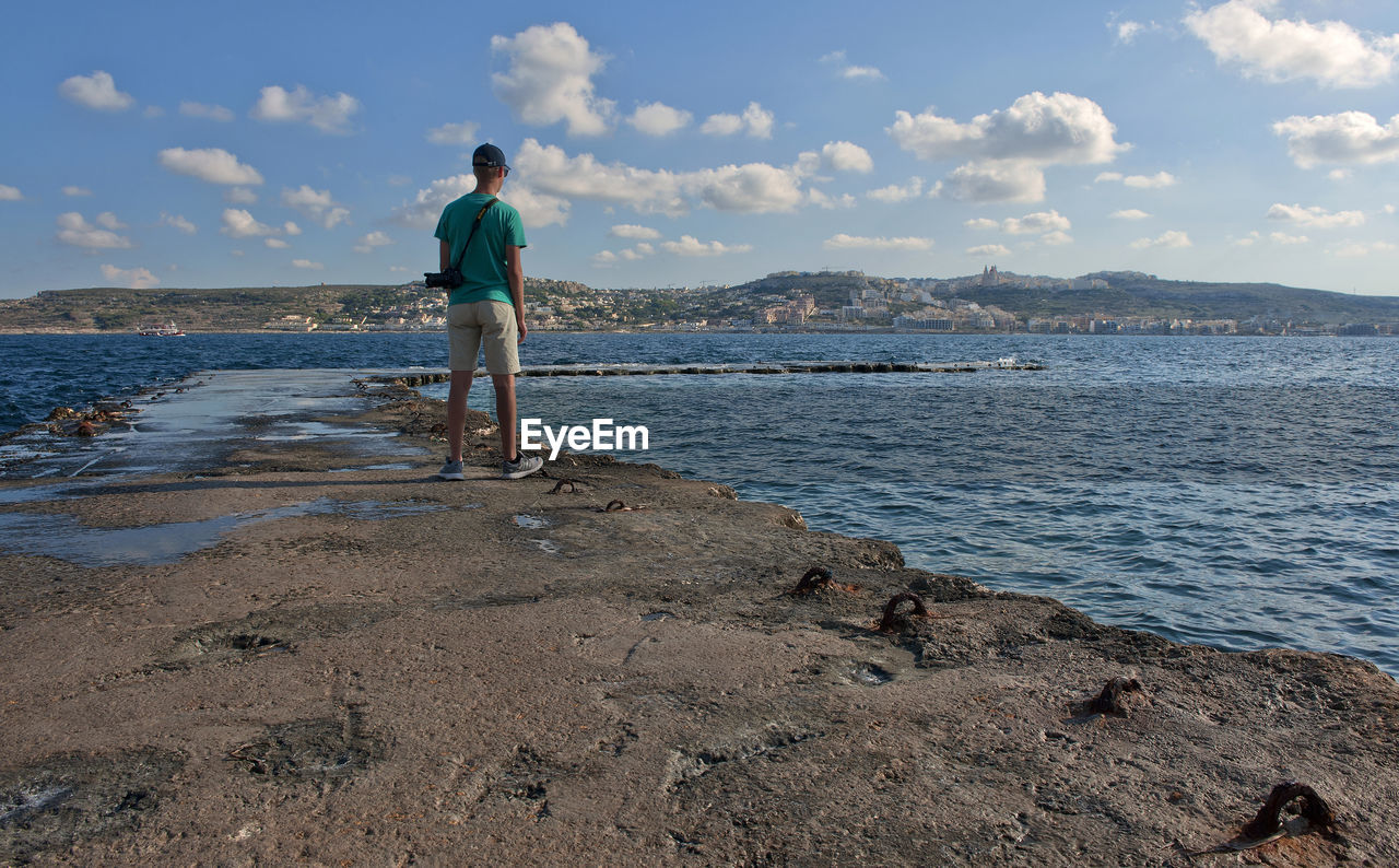 Rear view of man standing on beach against sky