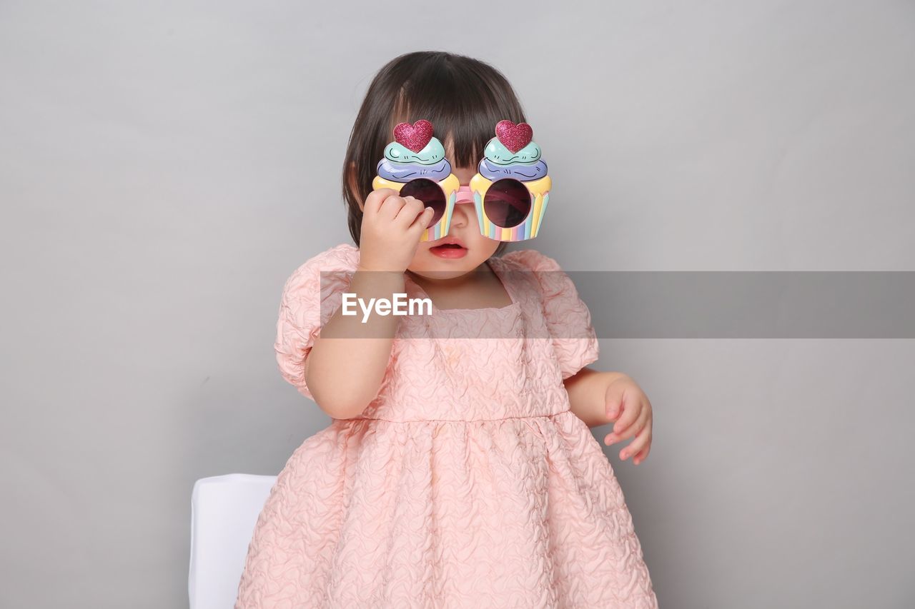 Little girl wearing sunglasses while standing against wall