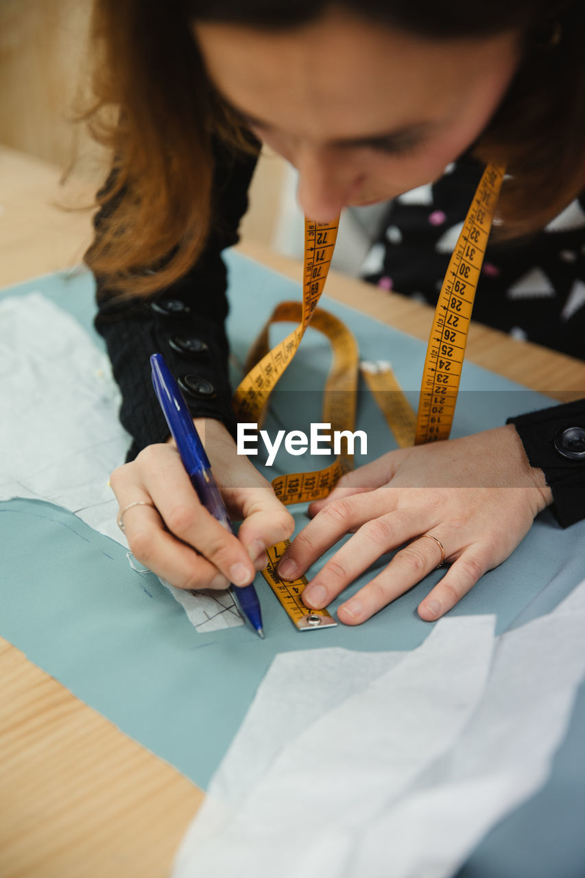 Adult lady using tape to measure garment part on table during work in professional dressmaking workshop