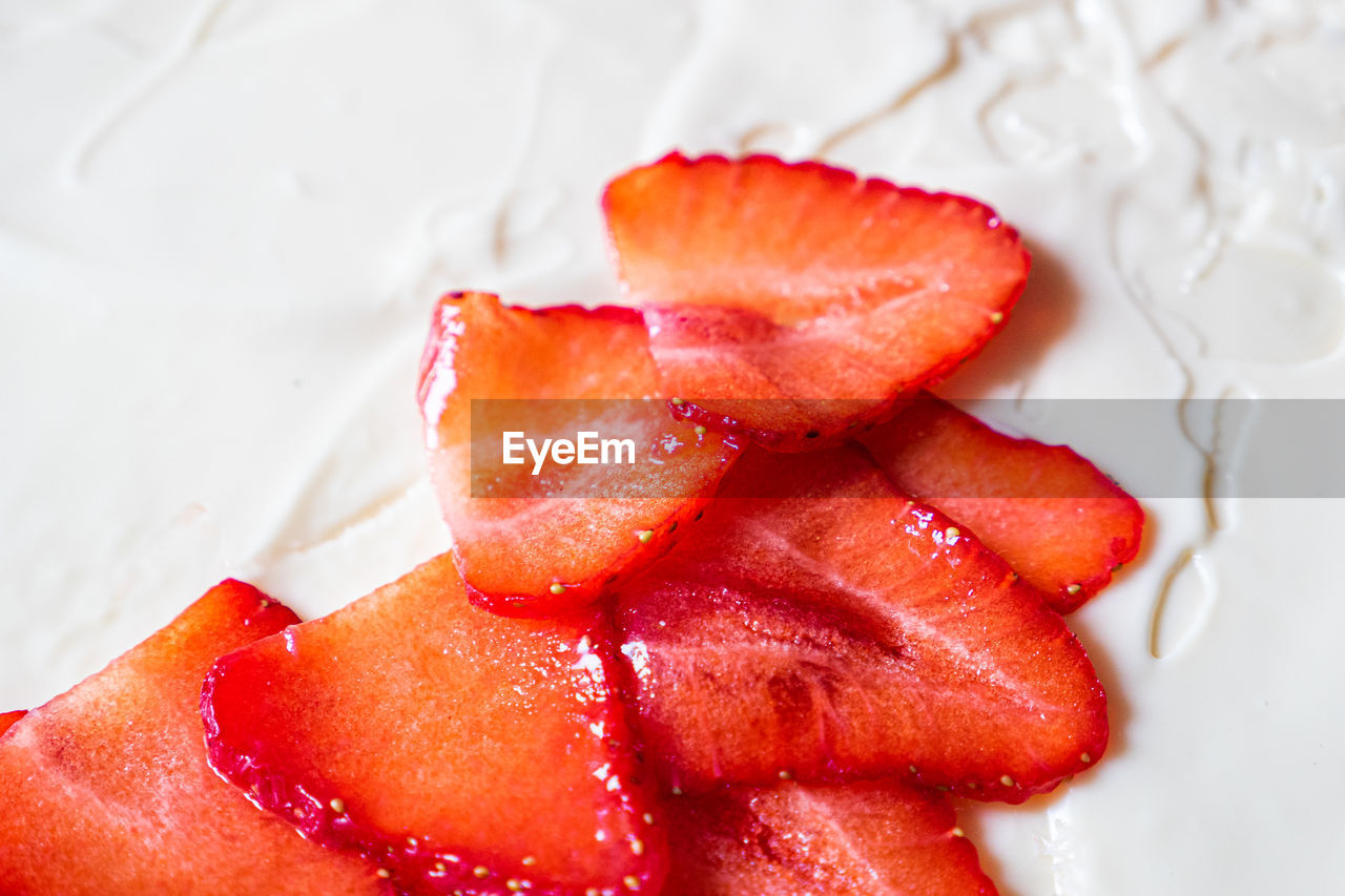 Red strawberry pieces on white cream background. top down view. close up.