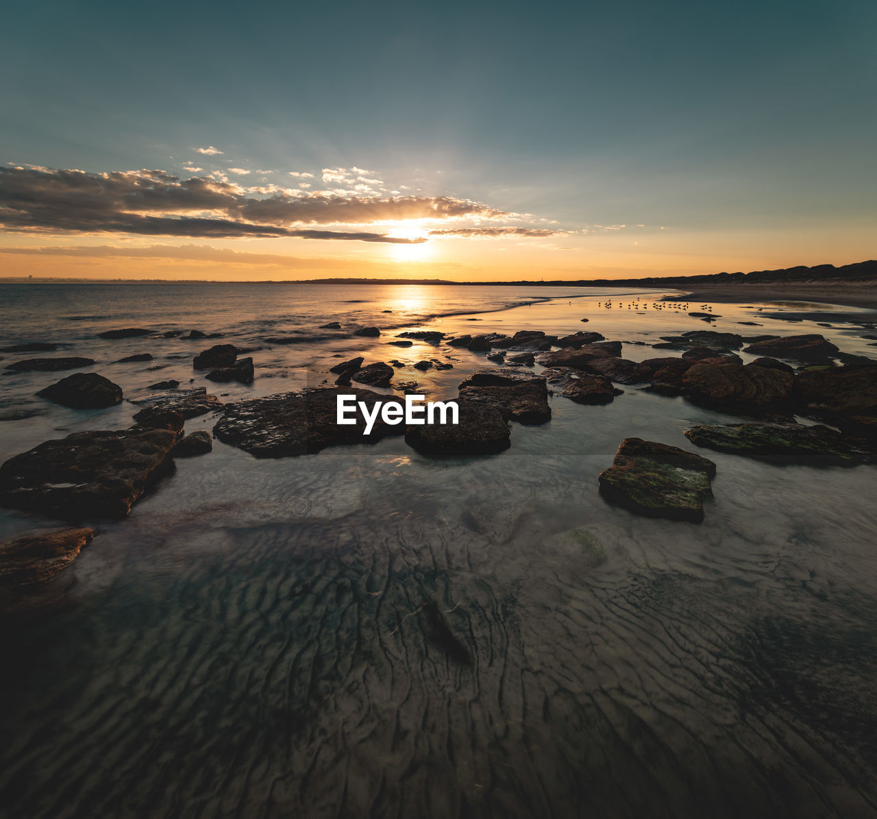 Wide angle long exposure shot of textured sand and rock formation on beach during sunset