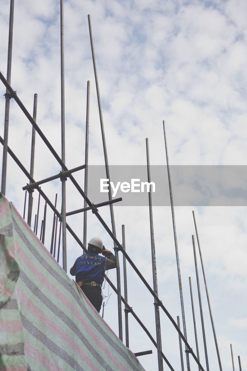 Low angle view of man standing on scaffolding against sky