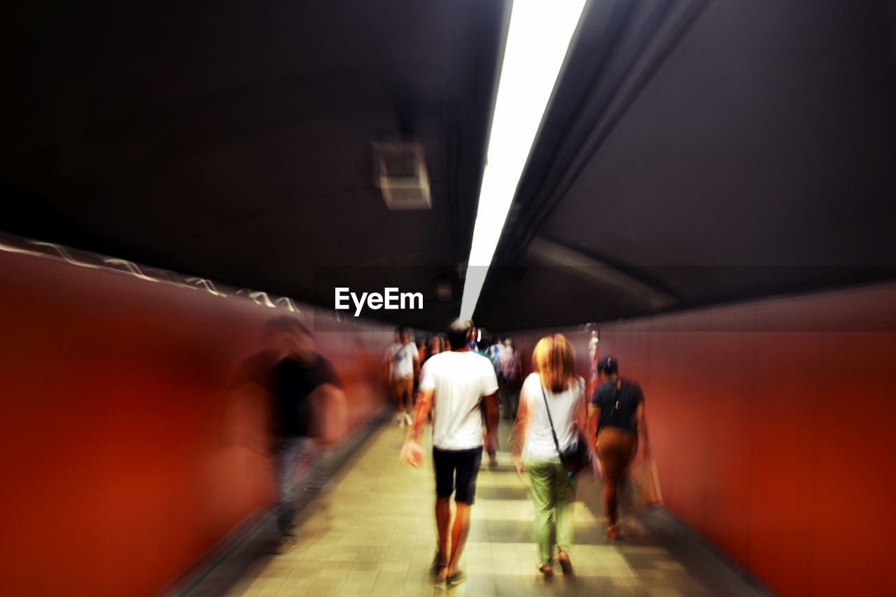 REAR VIEW OF PEOPLE WALKING IN SUBWAY TUNNEL