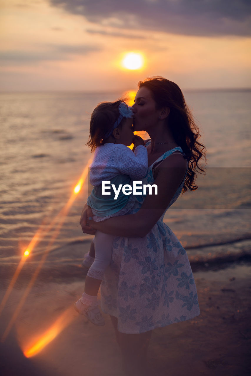 Mother holding her child at sunset by the sea