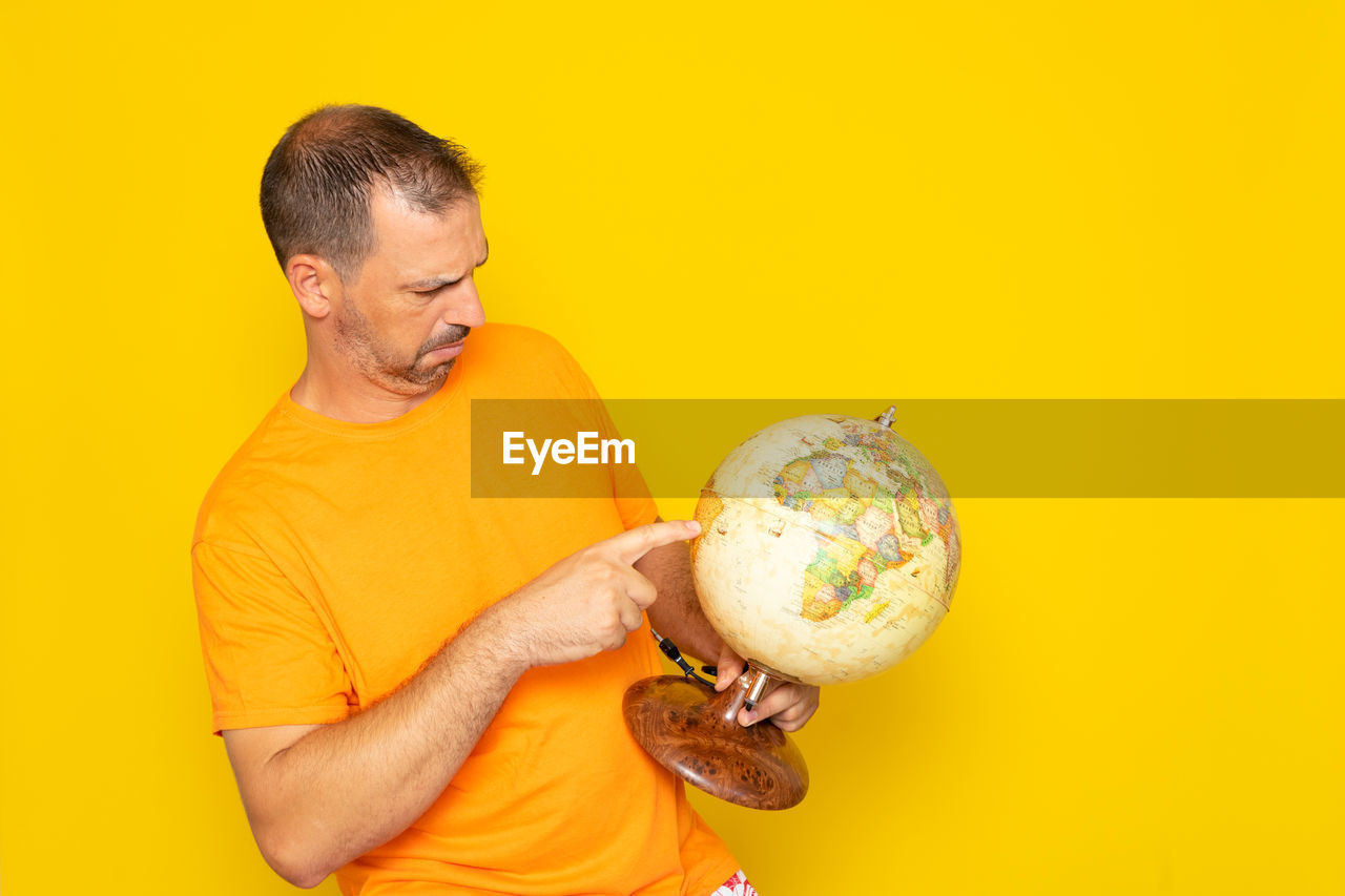 colored background, yellow, adult, studio shot, one person, yellow background, men, holding, indoors, person, waist up, copy space, ball, emotion, mature adult, portrait, smiling, casual clothing, orange color, clothing, food