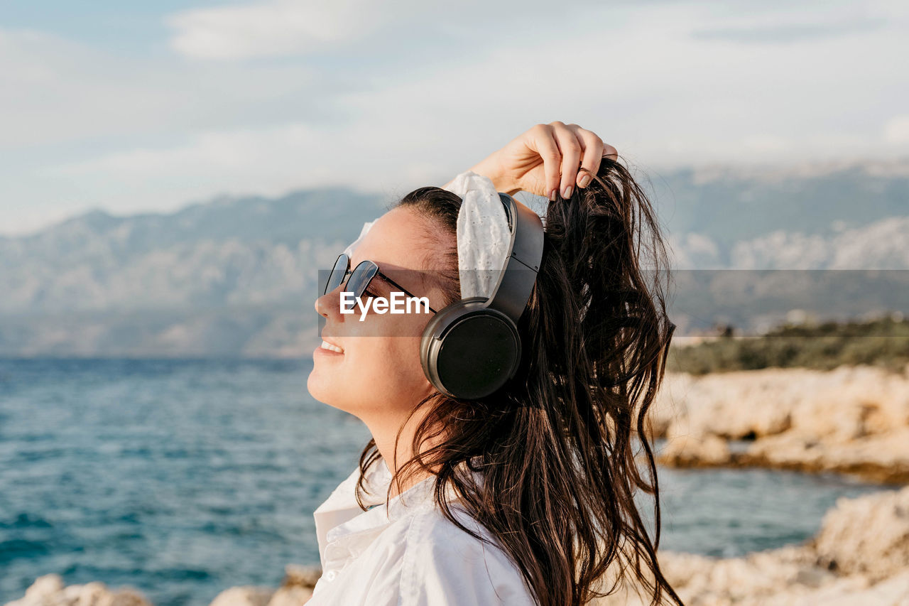 Side view of young woman in white shirt listening to music on headphones. summer, beach, lifestyle.