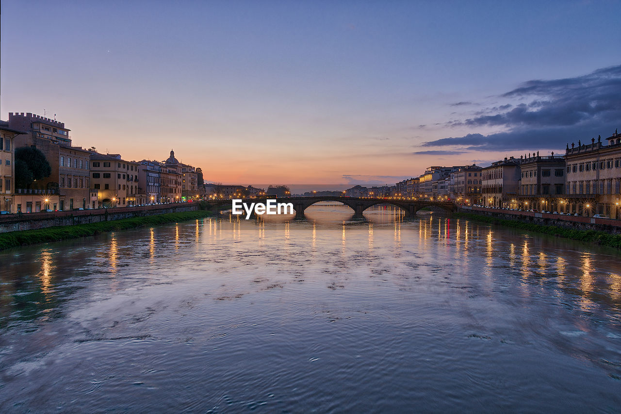 Bridge over river against buildings during sunset