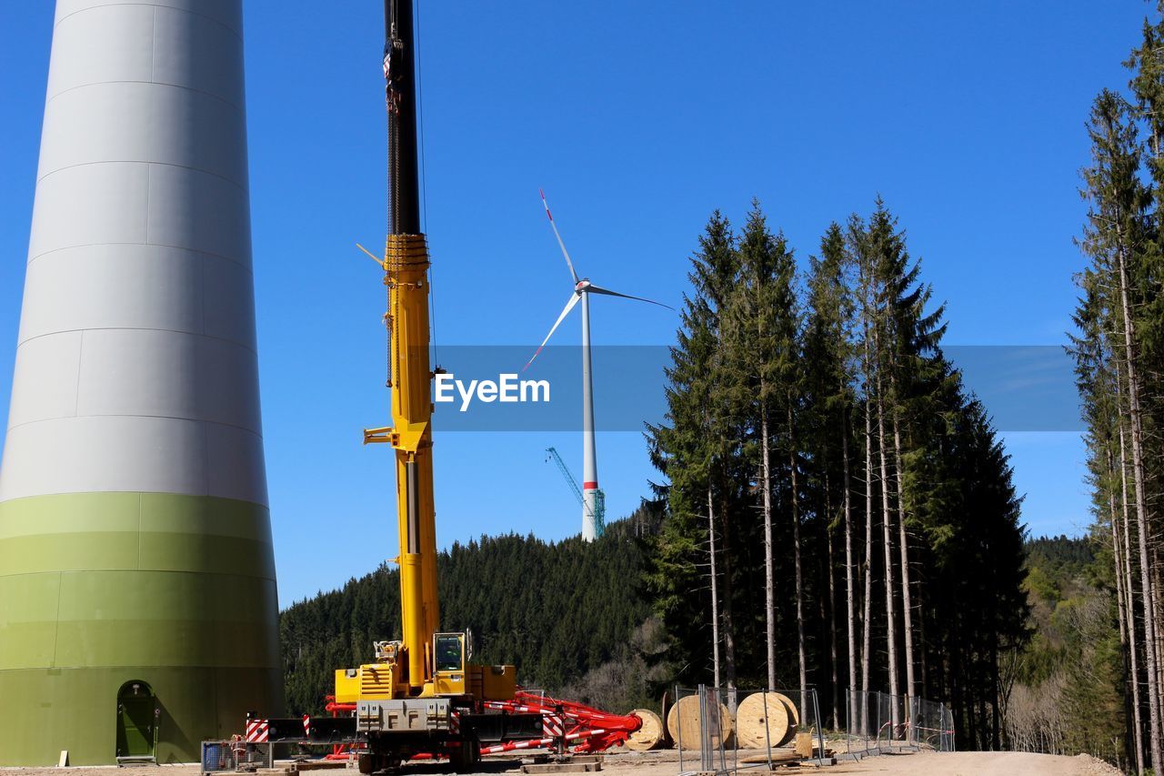 Construction machine by windmills on field against clear blue sky