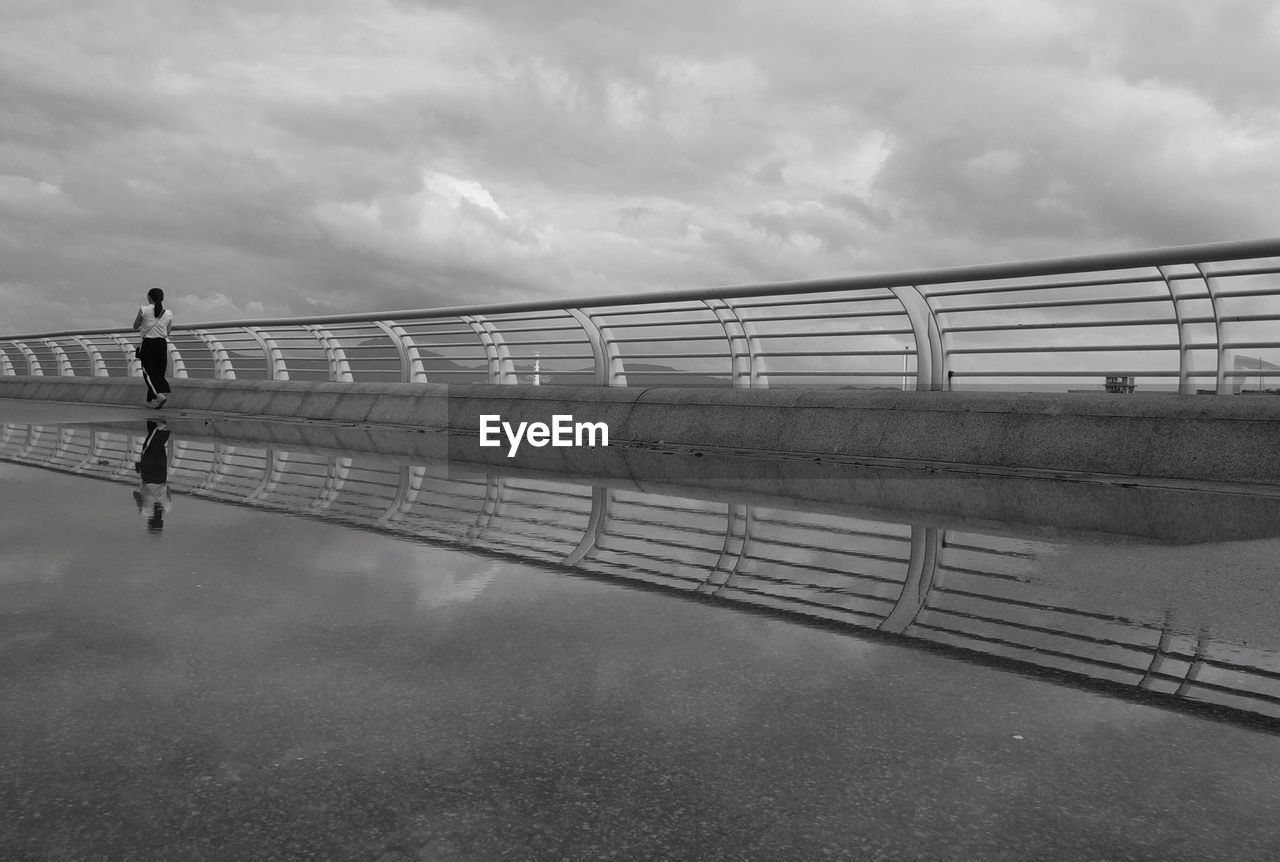 MAN WALKING ON BRIDGE AGAINST SKY