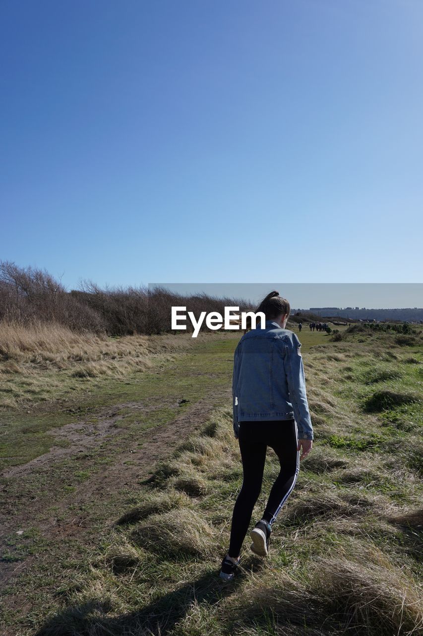 Rear view of girl walking on land against clear sky