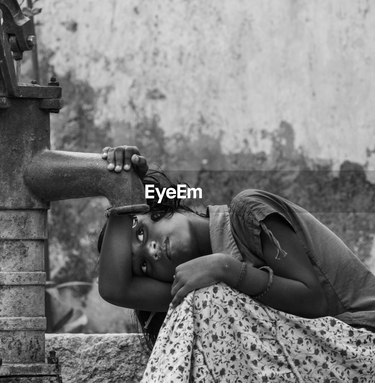 Girl trying to drink water from hand pump against wall