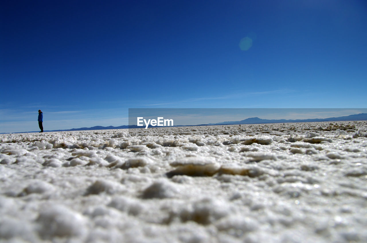 Surface level shot of woman standing on land against clear blue sky