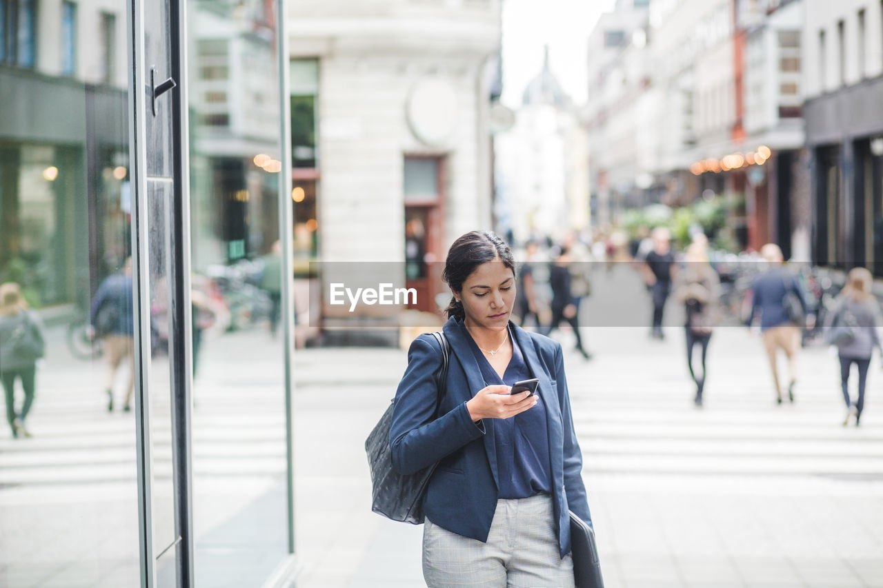 Businesswoman using phone while standing in city