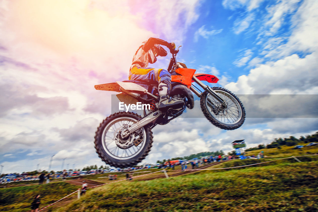 Low angle view of man riding motorcycle on field against cloudy sky