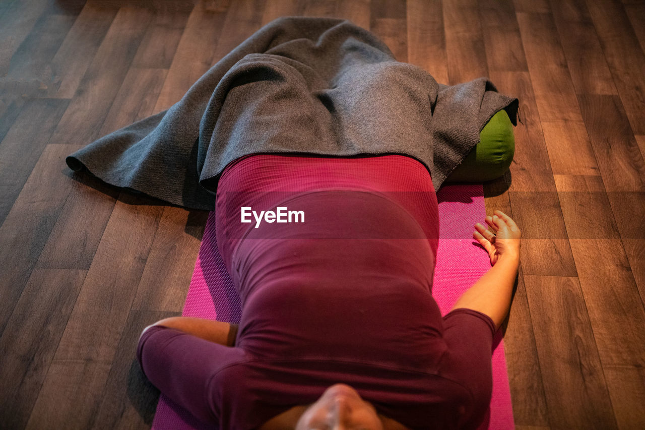 REAR VIEW OF WOMAN RELAXING ON FLOOR AT HOME