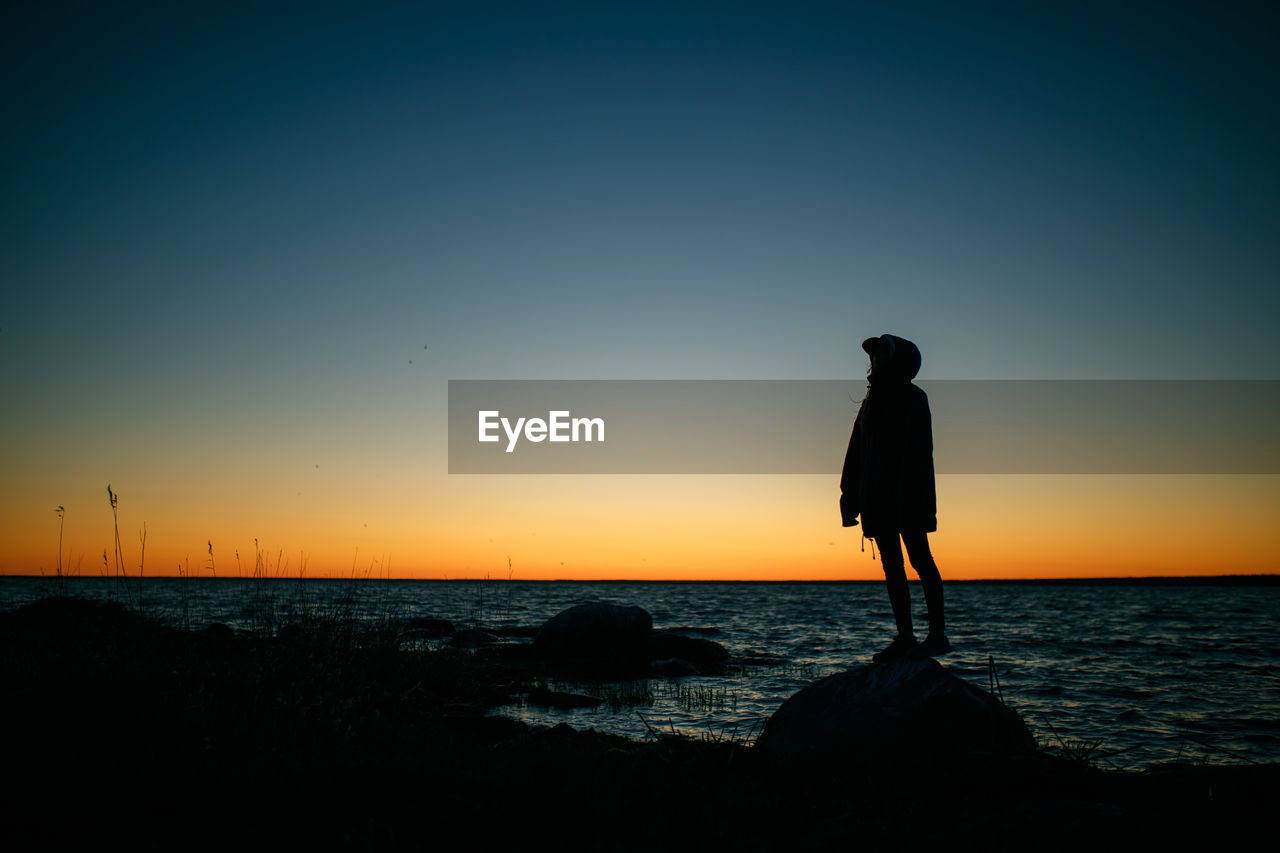 Silhouette man standing on beach against clear sky during sunset