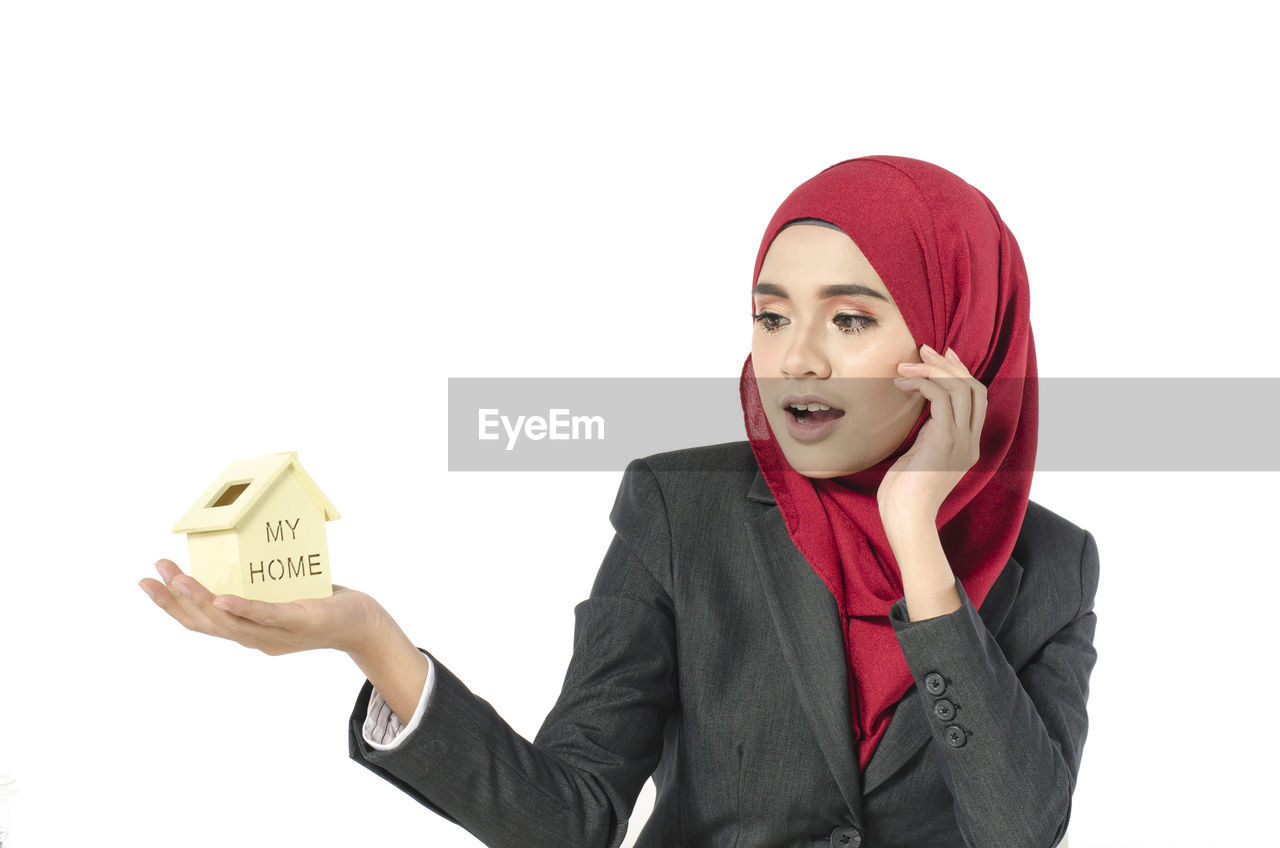 Surprised businesswoman holding house model against white background