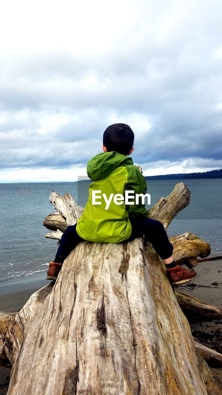 REAR VIEW OF A MAN OVERLOOKING SEA AGAINST SKY