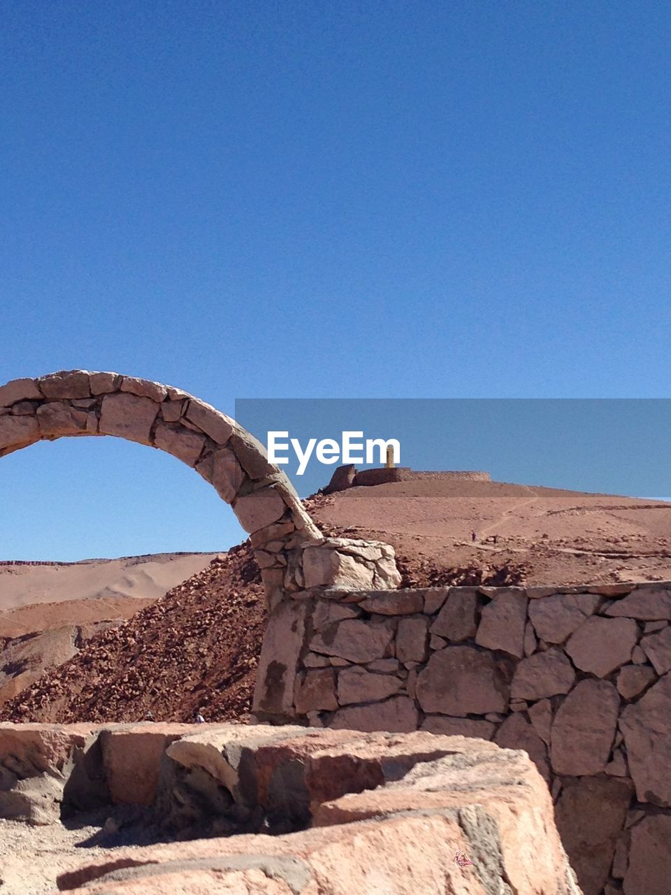 Arch by wall at desert against blue sky