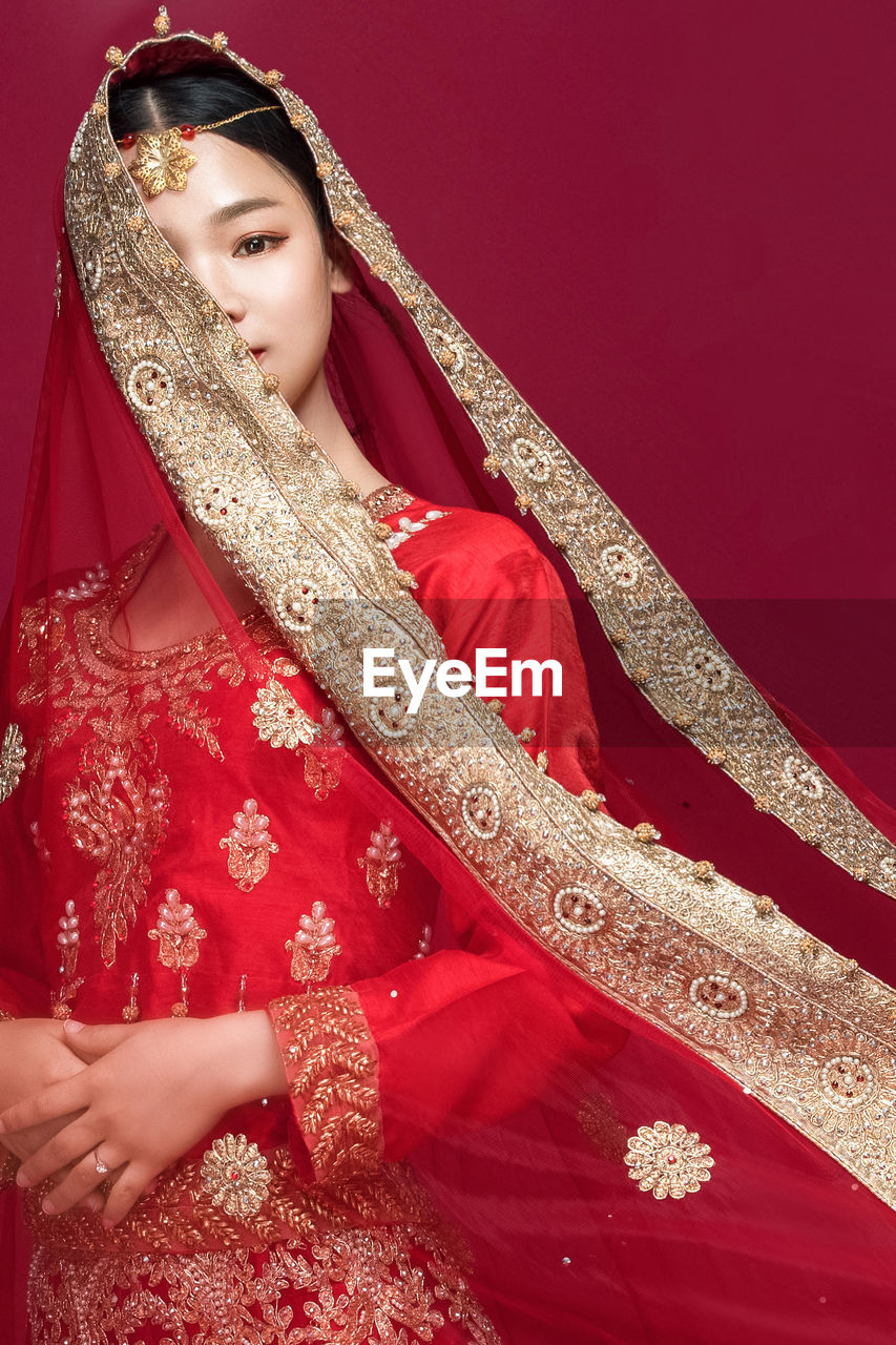 Portrait of beautiful young bride standing against red background