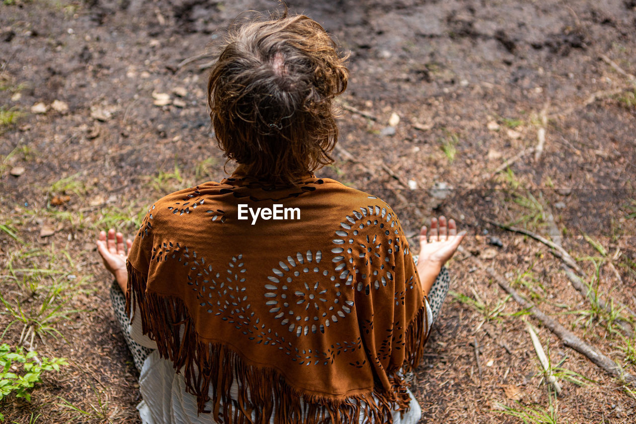 REAR VIEW OF WOMAN SITTING ON ROCK