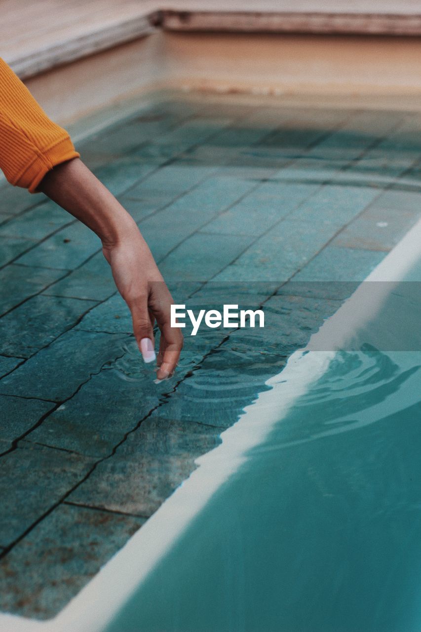 Cropped hand of woman touching swimming pool