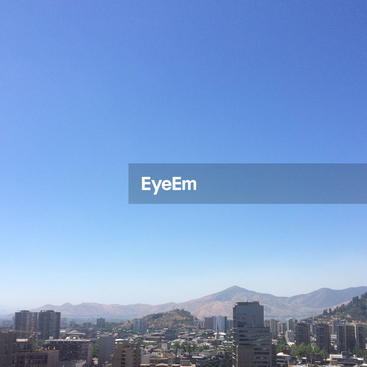 Buildings and mountains against clear blue sky