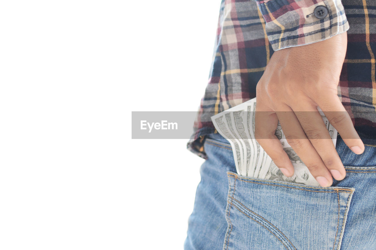 Midsection of man putting paper currencies in back pocket against white background