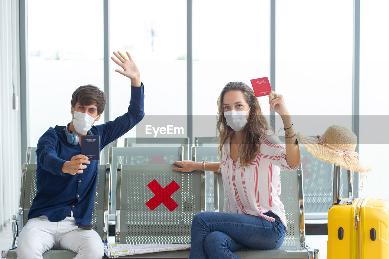 Portrait of smiling couple wearing flu mask showing passport at airport