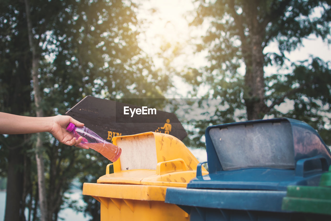 Cropped image woman throwing bottle in garbage bin