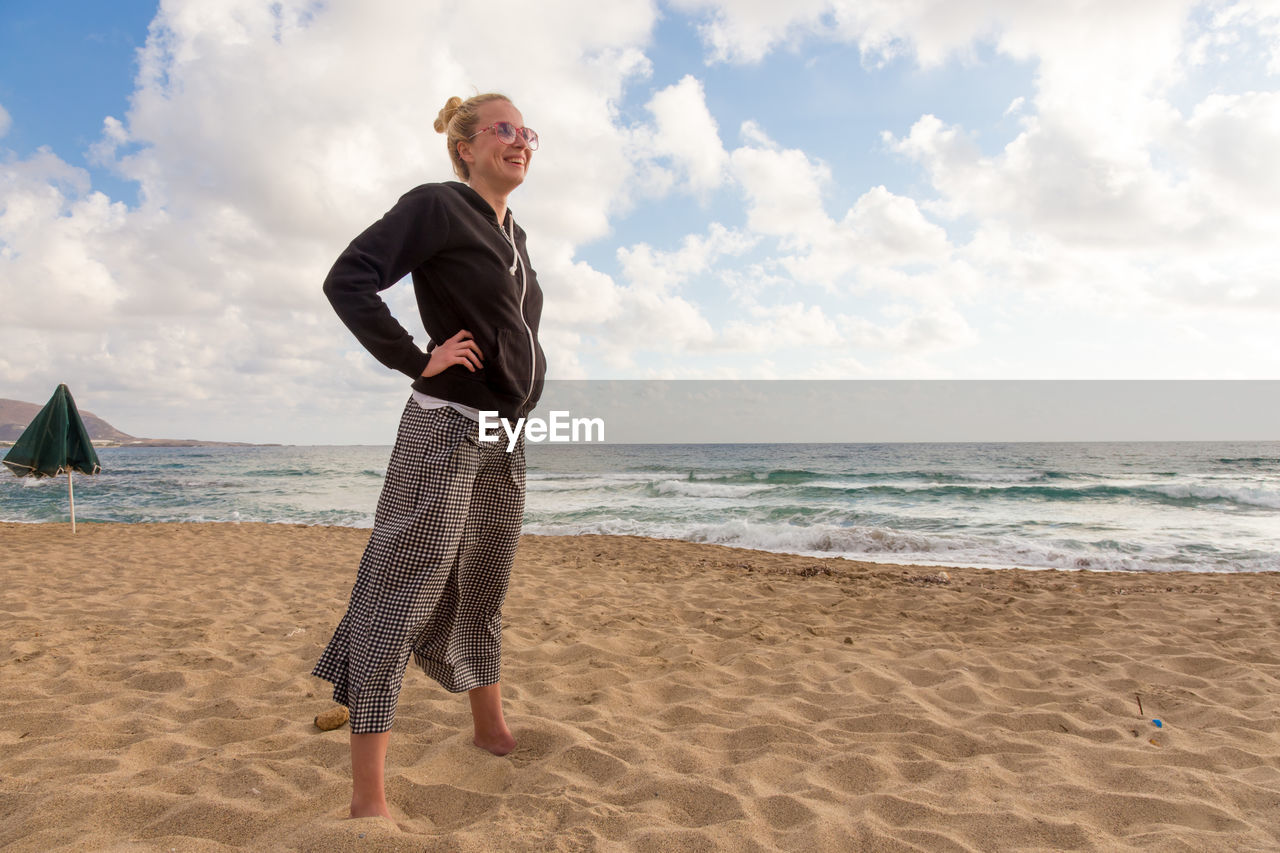 Full length of smiling woman on beach against sky