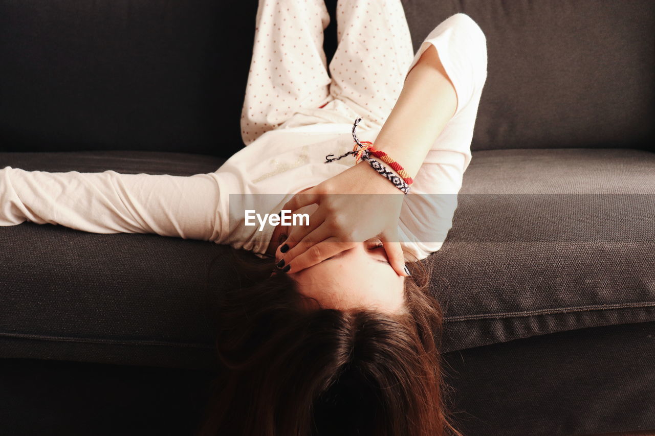 MIDSECTION OF A WOMAN SITTING ON SOFA AT HOME