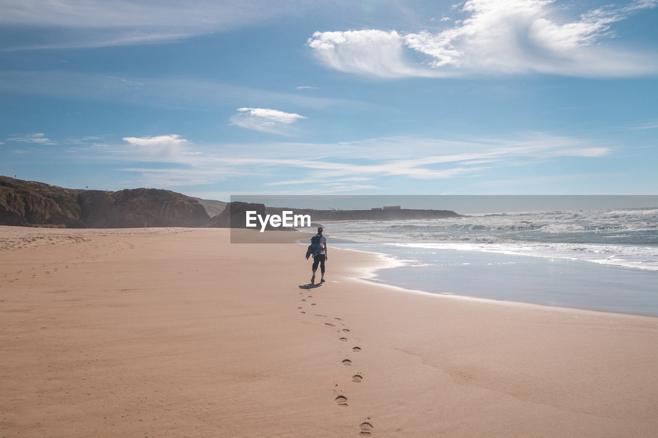 rear view of woman walking on beach against sky