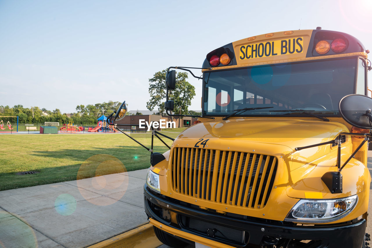 Front view of yellow school bus parked along sidewalk in front of school playground