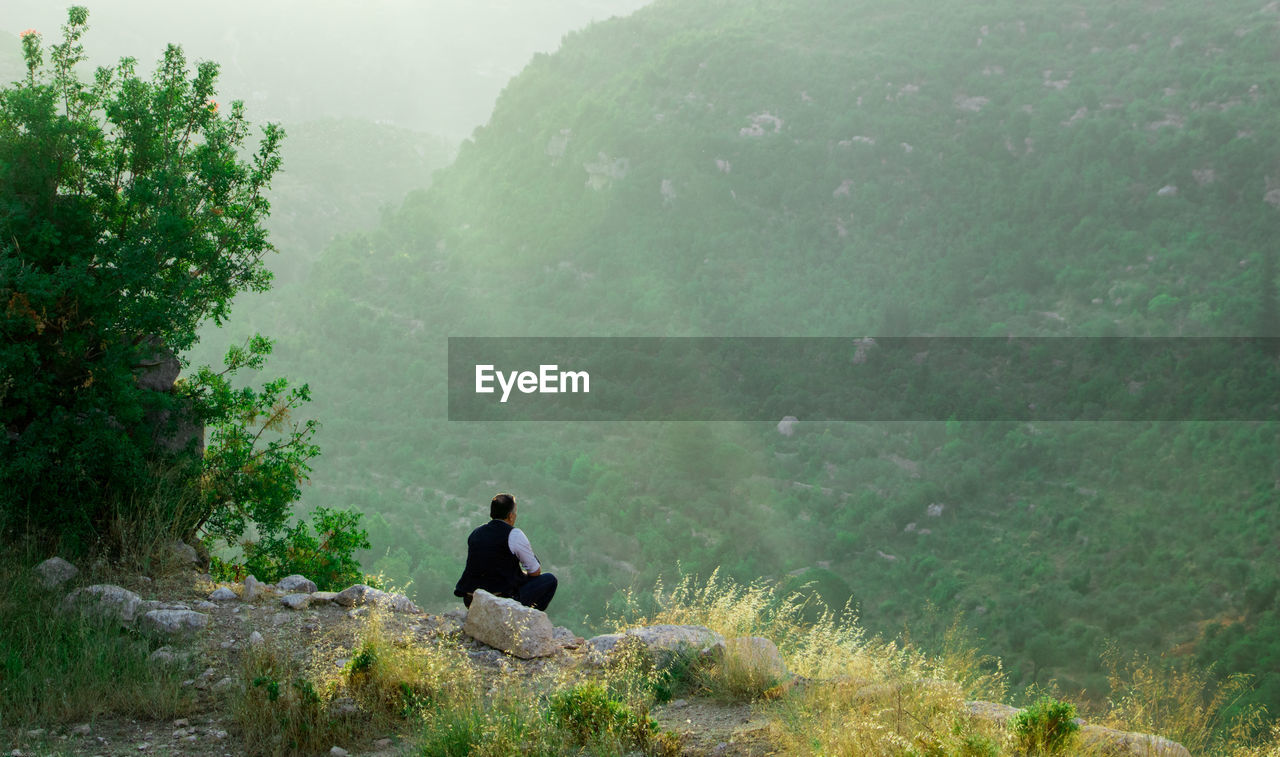 Man sitting on rock against mountain