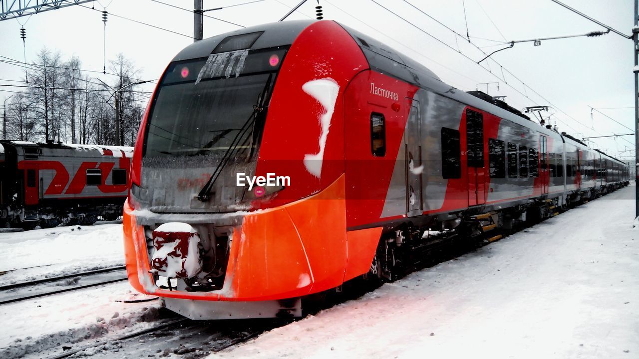 Modern trains at snow covered field against sky