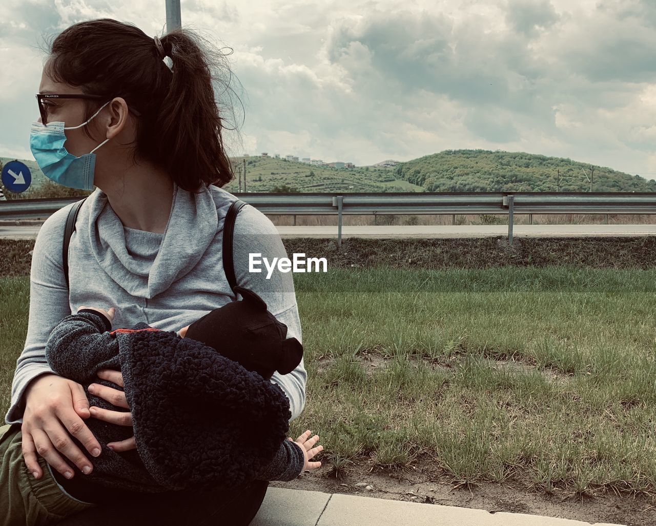 YOUNG WOMAN SITTING ON FIELD AGAINST SKY