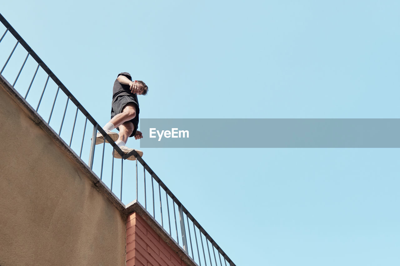From below of male standing on metal railing of building and preparing for performing parkour trick