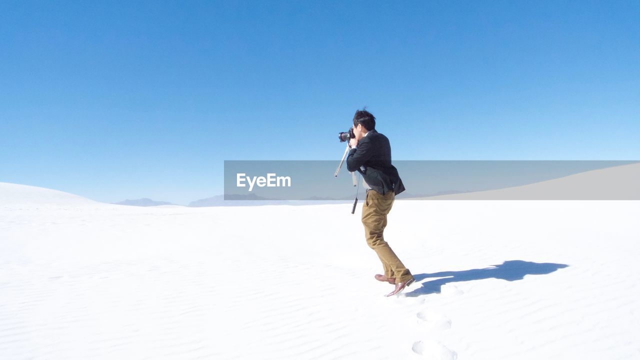 Full length of man photographing against clear sky