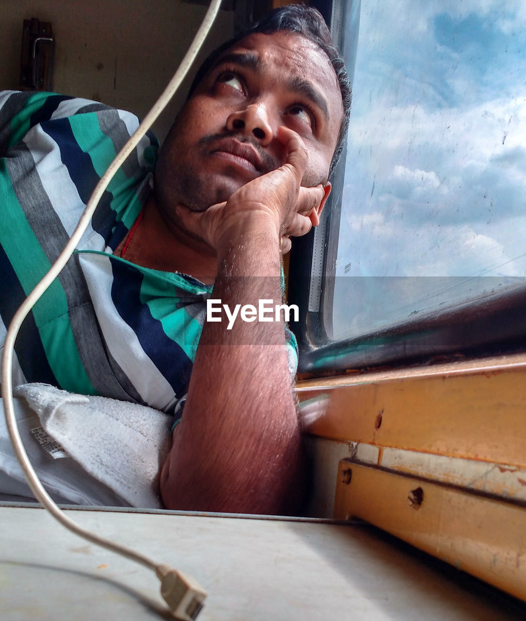 Thoughtful man looking up while lying by glass window