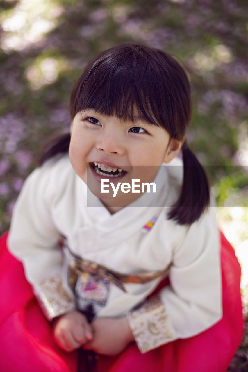 Korean girl child in a national costume walks in a garden with cherry blossoms in spring