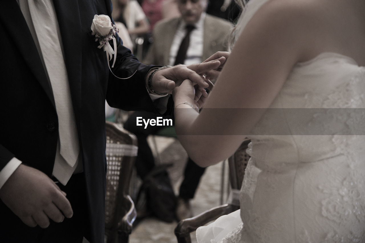 Midsection of bride inserting wedding ring in bridegroom finger