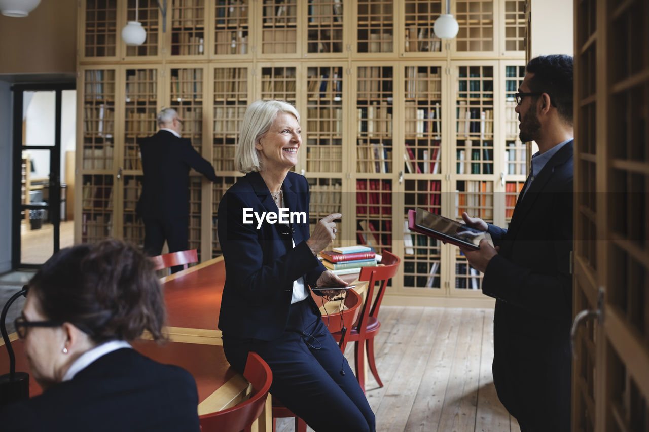 Happy senior lawyer discussing with coworker in board room at library