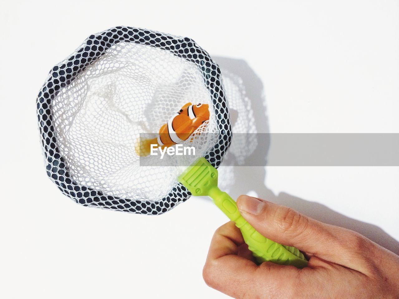 Cropped image of woman holding toy clown fish in net over white background